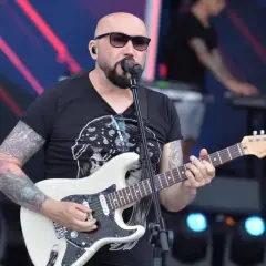 Artysta z tatuażami gra na gitarze, śpiewając do mikrofonu. Koncertowy klimat, jakby to były **kombi piosenki alfabetycznie**.