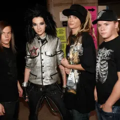 Członkowie Tokio Hotel pozują do zdjęcia. Bill Kaulitz w błyszczącej kurtce, Tom Kaulitz w czapce i z dredami, a obok nich Georg Listing i Gustav Schäfer.