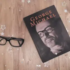 Okładka książki o George'u Michaelu, obok okulary i gwiazdki. Idealna lektura dla fanów jego albumów.