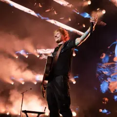 Ed Sheeran w Polsce, na scenie z gitarą, w otoczeniu dymu i świateł, pozdrawia publiczność.