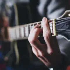 Dłoń grająca akord na gitarze. Muzyka tworzy niepowtarzalny zespół z korą drzewa, z którego wykonano instrument.