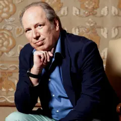 Hans Zimmer, kompozytor znany z muzyki do filmów, siedzi w fotelu, opierając podbródek na dłoni.