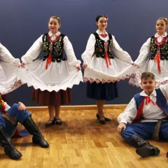 Dzieci w strojach ludowych, dziewczęta trzymają białe spódnice, chłopcy w niebieskich spodniach i kamizelkach, gotowi do tańca kołomyjka.