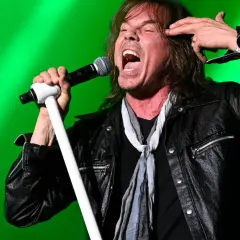 Wokalista Europe, Joey Tempest, w rockowym stylu, z mikrofonem w dłoni, na tle zielonej sceny.