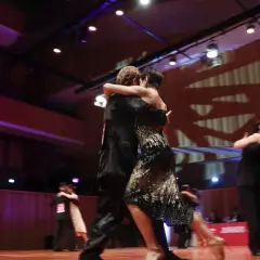 Para tańczy tango milonga, w tle widać innych tancerzy i scenę. Kompozytor mógłby czerpać inspirację z tej pasji.