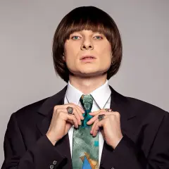 Ralph Kaminski, znany z oryginalnego stylu i charyzmy, poprawia krawat. Jego wzrost jest imponujący, podobnie jak talent.