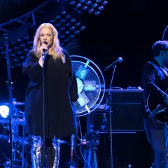 Wokalistka w błyszczących kozakach śpiewa na scenie, obok gitarzysta. W tle perkusista i scenografia z wentylatorami. To świetne hey utwory!