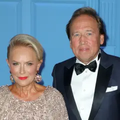 Elegancka para: kobieta w błyszczącej sukni i mężczyzna w smokingu na tle niebieskiej ściany.