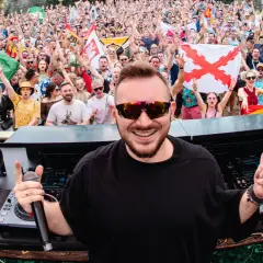 Skytech DJ w akcji, rozkręca tłum na festiwalu. W tle widać flagi i radosnych ludzi.