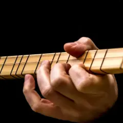 Dłoń na gryfie gitary, palce dociskają struny. Idealny moment, by dowiedzieć się, jak nastroić gitarę.