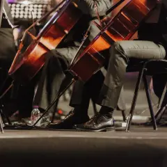 Orkiestra grająca muzykę filmową. Widoczne fragmenty instrumentów i eleganckie buty muzyków.