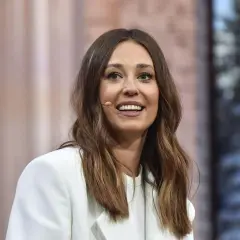 Uśmiechnięta Izabella Krzan w białej marynarce, jej wzrost jest imponujący, a włosy opadają na ramiona.