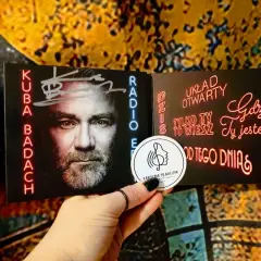 Kuba Badach z autografem na okładce płyty. Neonowe napisy "Dziś układ otwarty", "Tylko ty to wiesz", "Gdzie ty jesteś", "Od tego dnia".