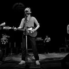 Koncert polskich zespołów punkowych. Wokalista z gitarą na pierwszym planie, obok gitarzysta i saksofonista.