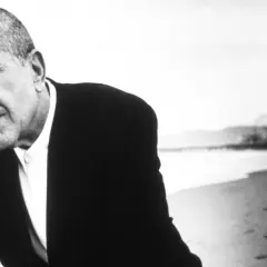 Leonard Cohen, w czerni i bieli, na plaży. Jego głębokie, poruszające utwory odzwierciedlają jego duszę.