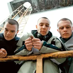 Trzech młodych mężczyzn, bohaterów filmu o paktofonice, pochyla się nad barierką. Jeden z nich trzyma w dłoniach bilet.