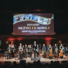 Koncert muzyki filmowej w Katowicach. Orkiestra symfoniczna na scenie pod ekranem z tytułem wydarzenia.