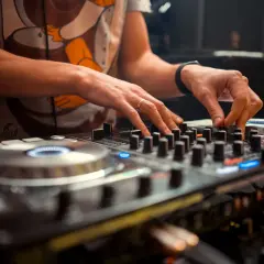 Dłonie DJ-a miksujące muzykę na sprzęcie. Widać pierścionek na palcu i zegarek. To polscy DJ-e tworzą rytm.