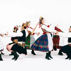 Tancerze w barwnych strojach ludowych, w tym w tradycyjnych strojach kujawiaków, tworzą taneczny krąg.
