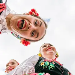 Uśmiechnięci młodzi ludzie w barwnych strojach ludowych, celebrujący polski folklor.