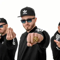 Trzech łobuzów członków w czarnych bluzach i czapkach z daszkiem, z okularami przeciwsłonecznymi, pozuje z gestami.