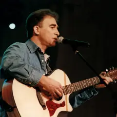 Seweryn Krajewski na scenie, gra na gitarze i śpiewa do mikrofonu. Jego muzyka wciąż porusza serca, a pytanie "czy Seweryn Krajewski żyje" jest niepotrzebne, bo jego twórczość jest wieczna.