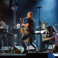 Koncert z utworami Krzysztofa Pendereckiego. Saksofonista w centrum, w tle orkiestra dęta i instrumenty smyczkowe.