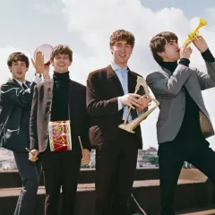 The Beatles w swoich eleganckich garniturach, grając na instrumentach, tworzą radosną atmosferę, jakby zapowiadali nowe utwory.