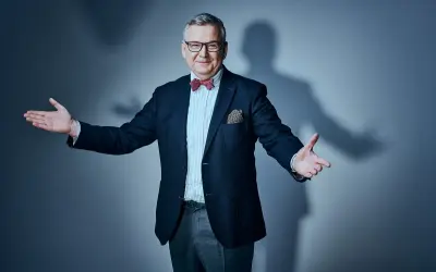 Artur Andruś, w eleganckim garniturze i muszce, gestykuluje, jakby opowiadał o swojej rodzinie.