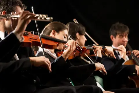 Orkiestra gra utwór, którego kompozytor z pewnością byłby dumny. Skupieni muzycy grają na skrzypcach i wiolonczeli.