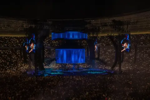 Koncert Dawida Podsiadło, tłum z zapalonymi światłami, wielkie ekrany z wizerunkiem artysty.