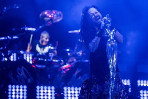 Jonathan Davis z Korn śpiewa z pasją, a w tle widać perkusistę. To scena z koncertu, jak z okładek korn albumy.