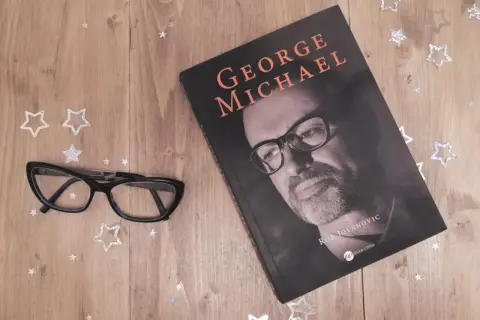 Okładka książki o George'u Michaelu, obok okulary i gwiazdki. Idealna lektura dla fanów jego albumów.