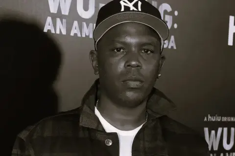 Członek Wu-Tang Clan w czapce z daszkiem i kratkowanej kurtce, na tle napisu "Wu-Tang: An American Saga".
