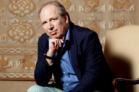 Hans Zimmer, kompozytor znany z muzyki do filmów, siedzi w fotelu, opierając podbródek na dłoni.