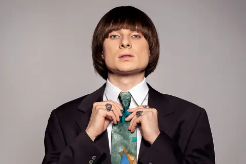 Ralph Kaminski, znany z oryginalnego stylu i charyzmy, poprawia krawat. Jego wzrost jest imponujący, podobnie jak talent.