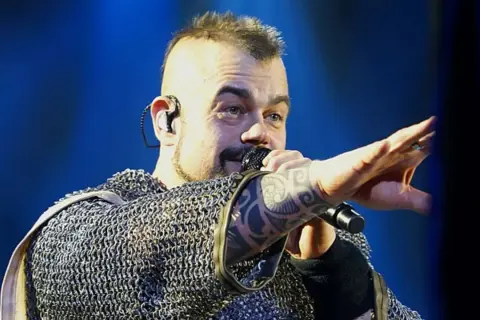 Wokalista Sabaton w kolczudze, z tatuażem na ręce, śpiewa na koncercie. Jego albumy to historie wojenne.
