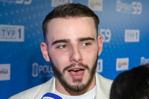 Krystian Ochman, z żoną u boku, pozuje na tle niebieskiej ścianki z logo TVP 1 i Opole 59.
