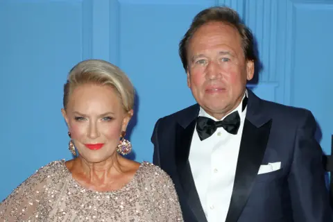 Elegancka para: kobieta w błyszczącej sukni i mężczyzna w smokingu na tle niebieskiej ściany.