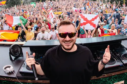 Skytech DJ w akcji, rozkręca tłum na festiwalu. W tle widać flagi i radosnych ludzi.