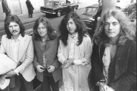 Czterech członków Led Zeppelin pozuje do zdjęcia na ulicy. John Bonham, John Paul Jones, Jimmy Page i Robert Plant wyglądają stylowo.