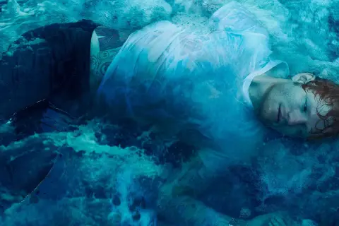 Ed Sheeran zanurzony w wodzie, jak na okładkach jego albumów. Woda tworzy surrealistyczną, błękitną mgłę wokół artysty.