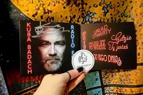 Kuba Badach z autografem na okładce płyty. Neonowe napisy "Dziś układ otwarty", "Tylko ty to wiesz", "Gdzie ty jesteś", "Od tego dnia".