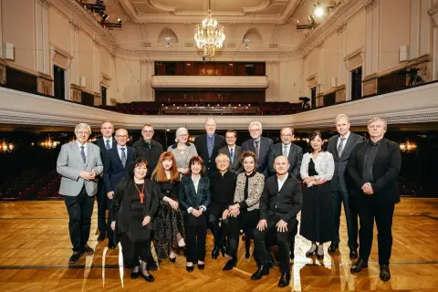Uczestnicy międzynarodowego konkursu pianistycznego im. Fryderyka Chopina pozują do wspólnego zdjęcia w eleganckiej sali koncertowej.