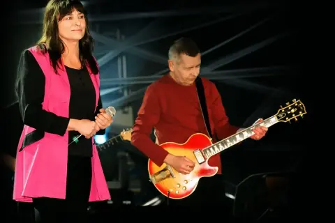 Kobieta z mikrofonem i mężczyzna grający na gitarze, członkowie zespołu Breakout, na scenie.