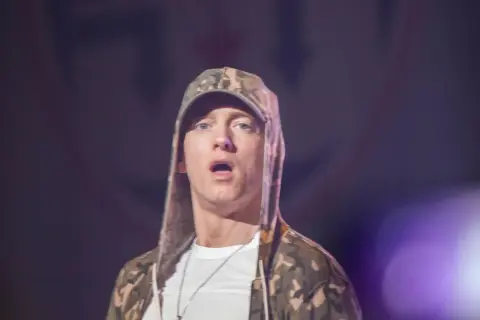 Eminem jak teraz wygląda, w bluzie z kapturem w kamuflażu i białej koszulce, z otwartymi ustami.