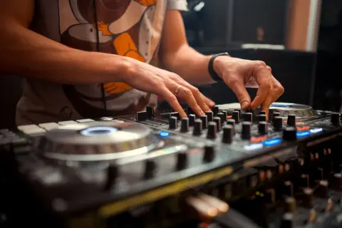 Dłonie DJ-a miksujące muzykę na sprzęcie. Widać pierścionek na palcu i zegarek. To polscy DJ-e tworzą rytm.