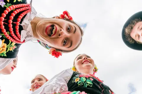 Uśmiechnięci młodzi ludzie w barwnych strojach ludowych, celebrujący polski folklor.