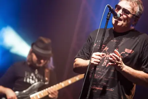 Wokalista Budki Suflera śpiewa na koncercie. W tle basista gra na gitarze. Piosenki Budki Suflera alfabetycznie to ich bogaty repertuar.