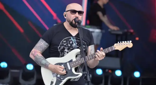 Artysta z tatuażami gra na gitarze, śpiewając do mikrofonu. Koncertowy klimat, jakby to były **kombi piosenki alfabetycznie**.